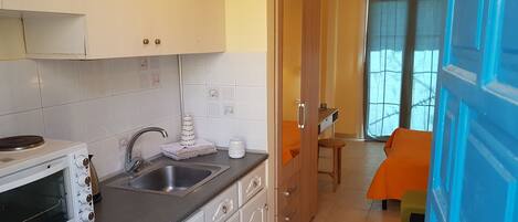 A compact kitchen with a microwave, sink, and cabinets. A dining area with a table and chairs is visible in the background.