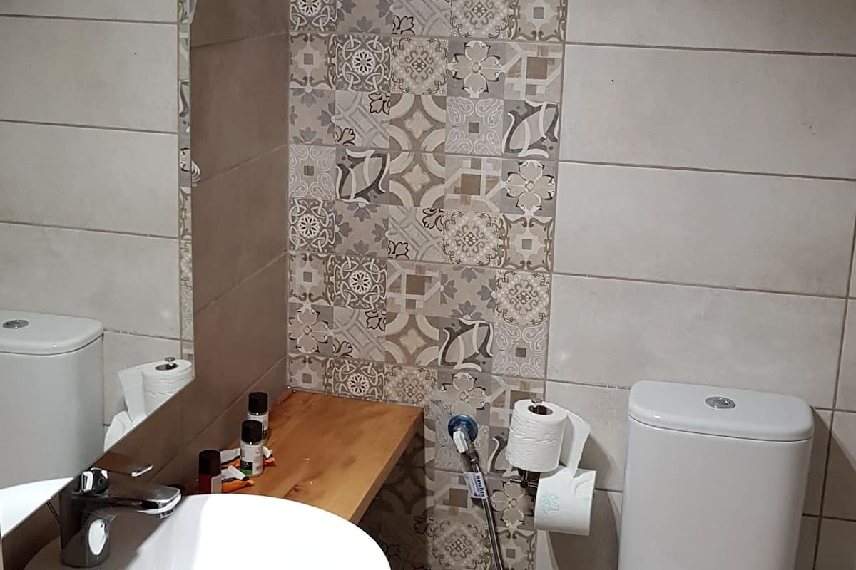 Un baño con lavamanos blanco, espejo, inodoro y azulejos decorativos en la pared.