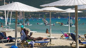 A beach with sun loungers and umbrellas, a sandy shore, and people engaging in water activities. - Nefeli Club (Lefkada)