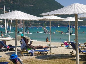 På stranden, solsenger, parasoller og brettseiling