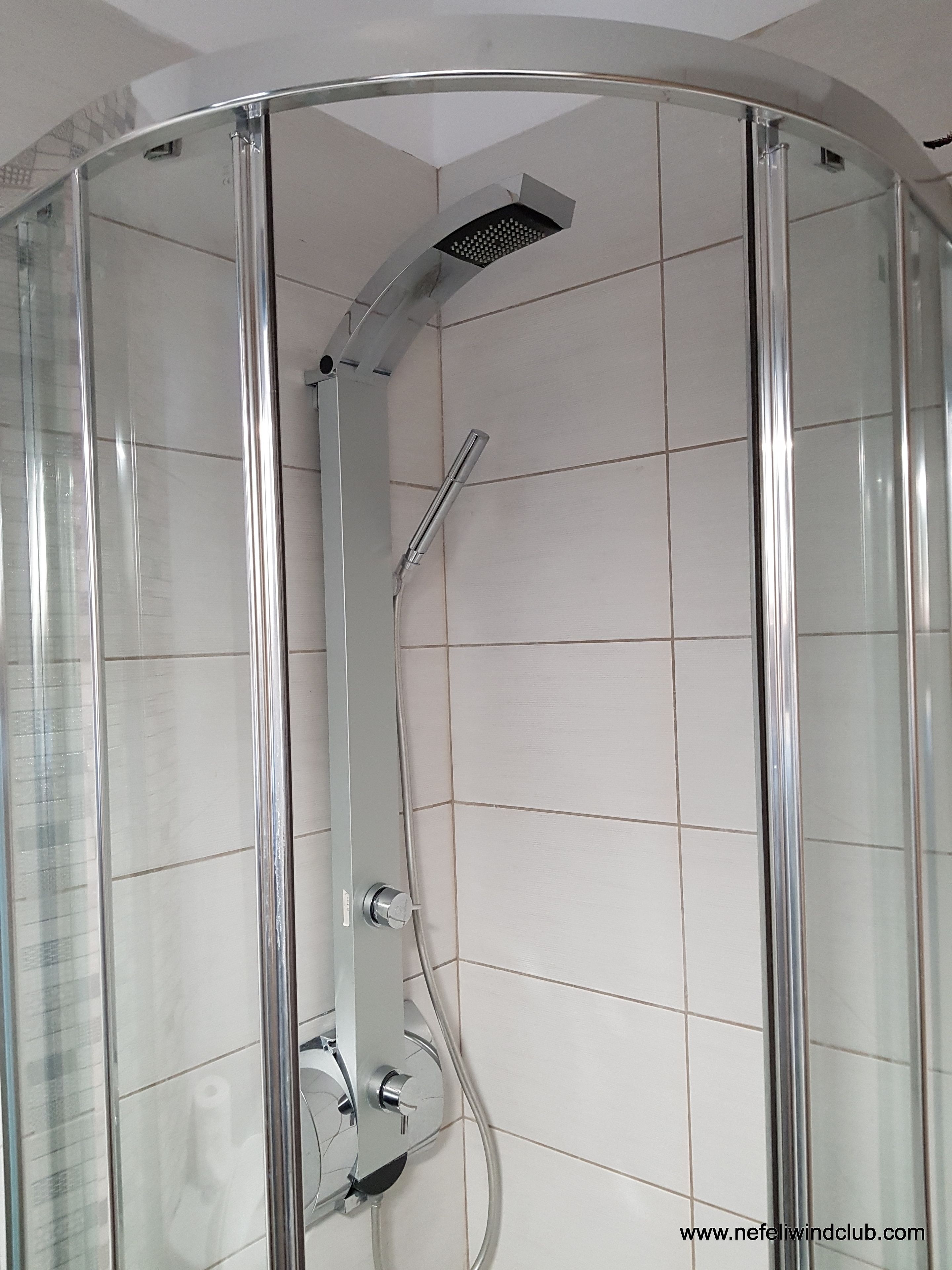 Een douche met glazen wand, een verchroomde douchekop en bedieningsknoppen.