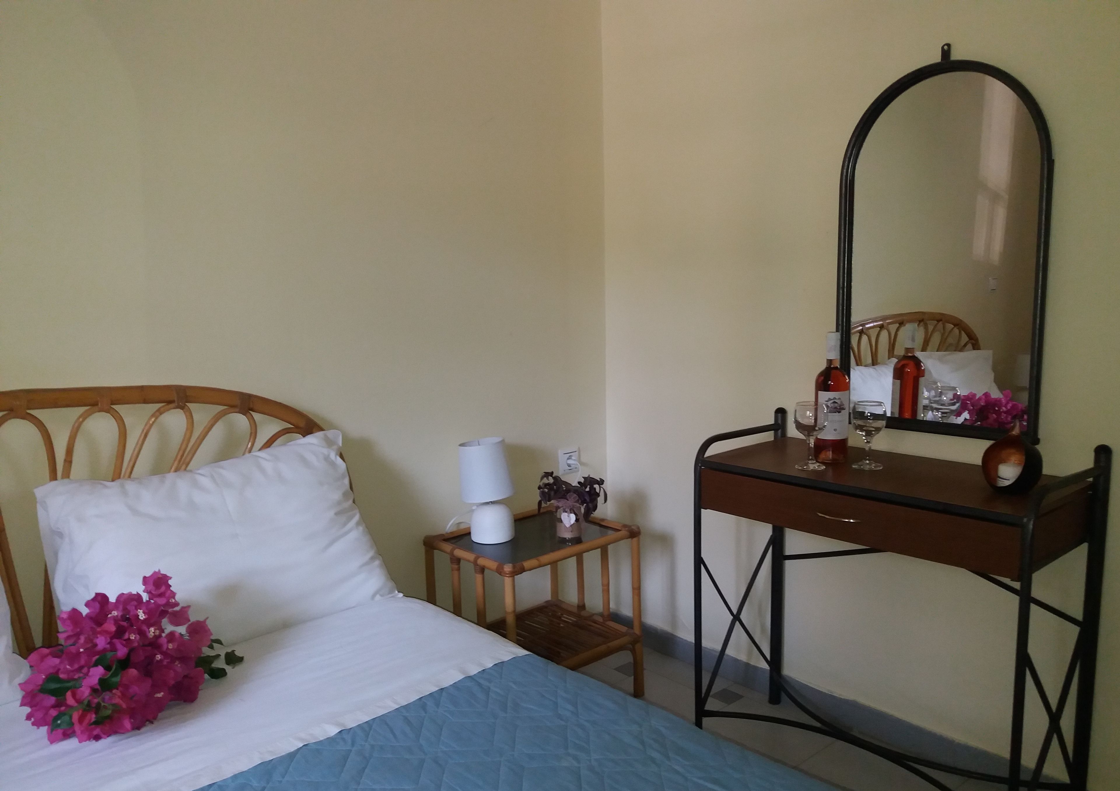 Una camera da letto con un letto, un comodino con una lampada, uno specchio e uno sgabello in legno.