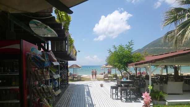 A wooden deck leading to a beach area with outdoor seating and umbrellas. - Nefeli Club (Lefkada)