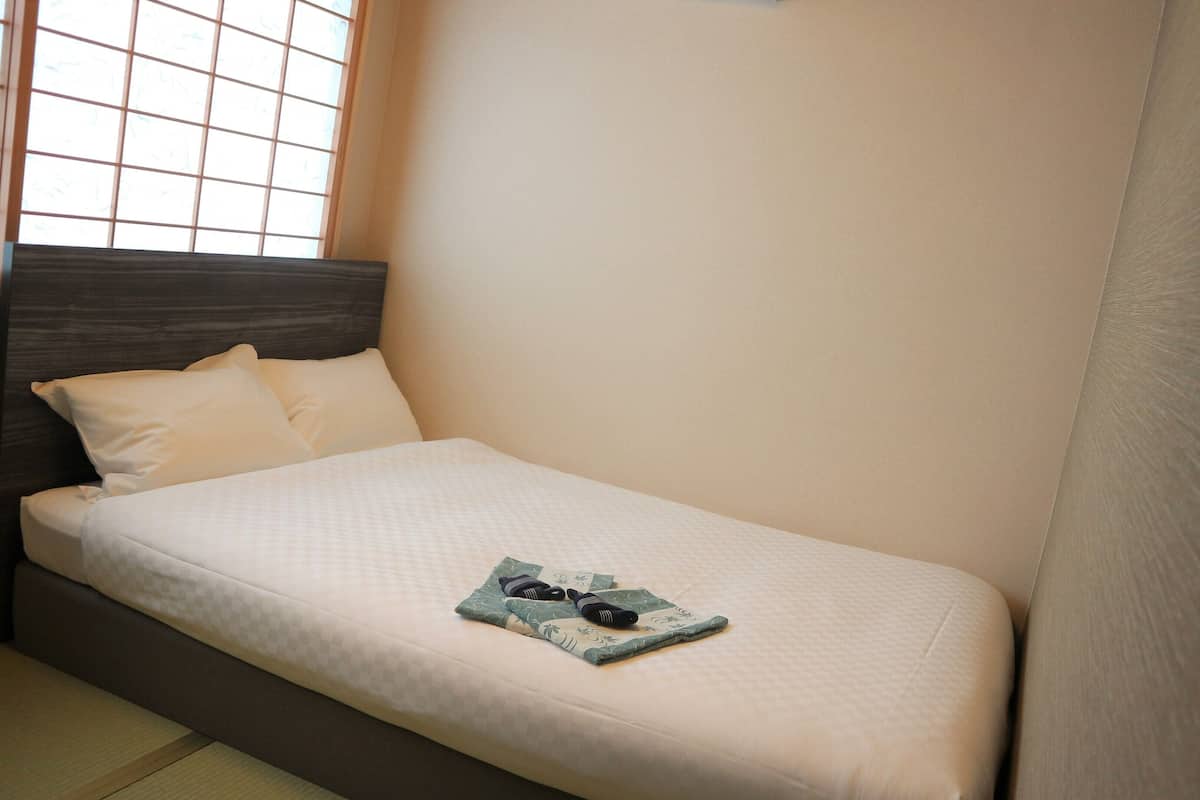 Una cama individual con colchón a cuadros, dos almohadas y una mesita con una toalla doblada y un secador de pelo.