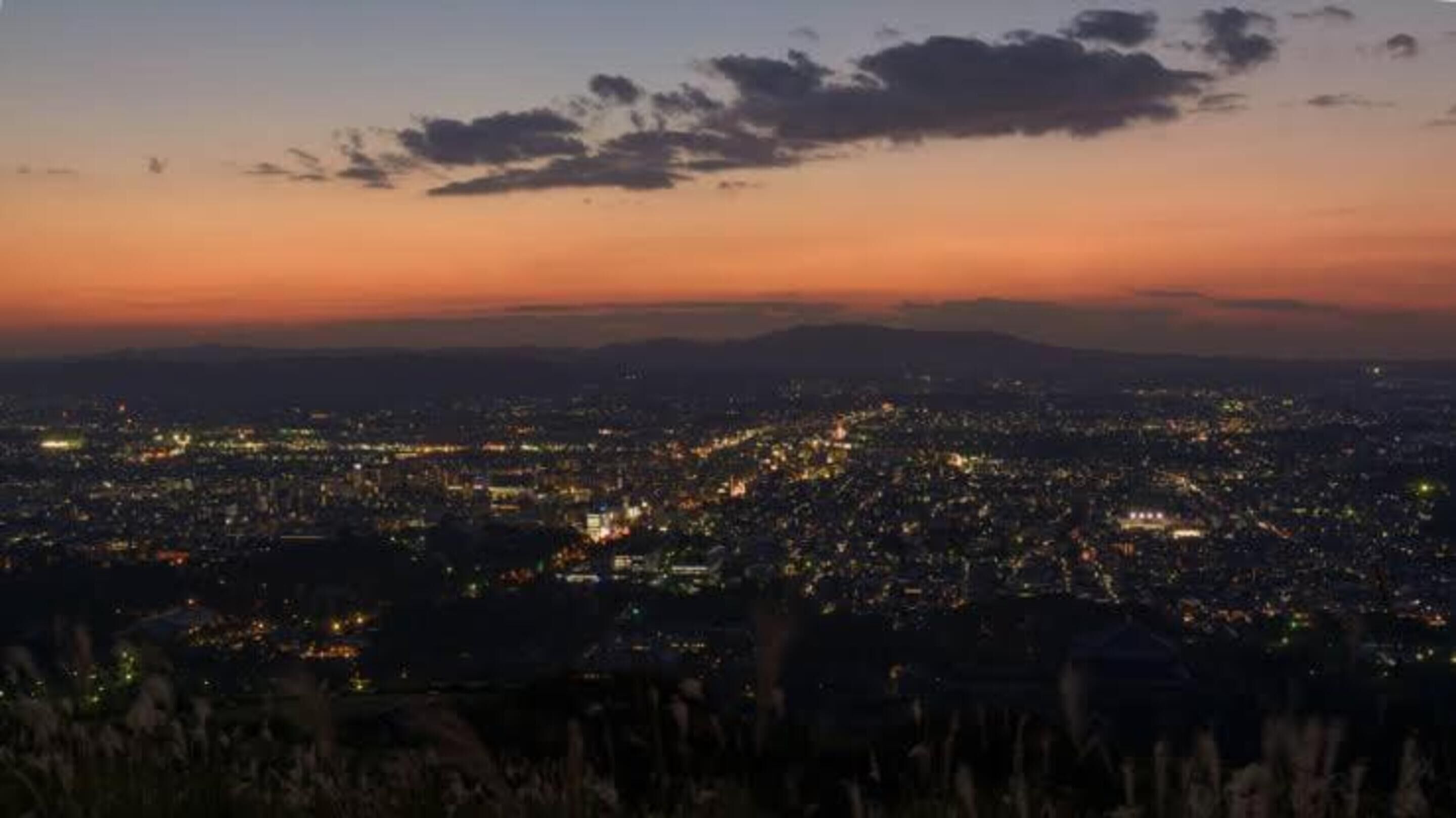 A nighttime cityscape with a view of the city lights and distant mountains.