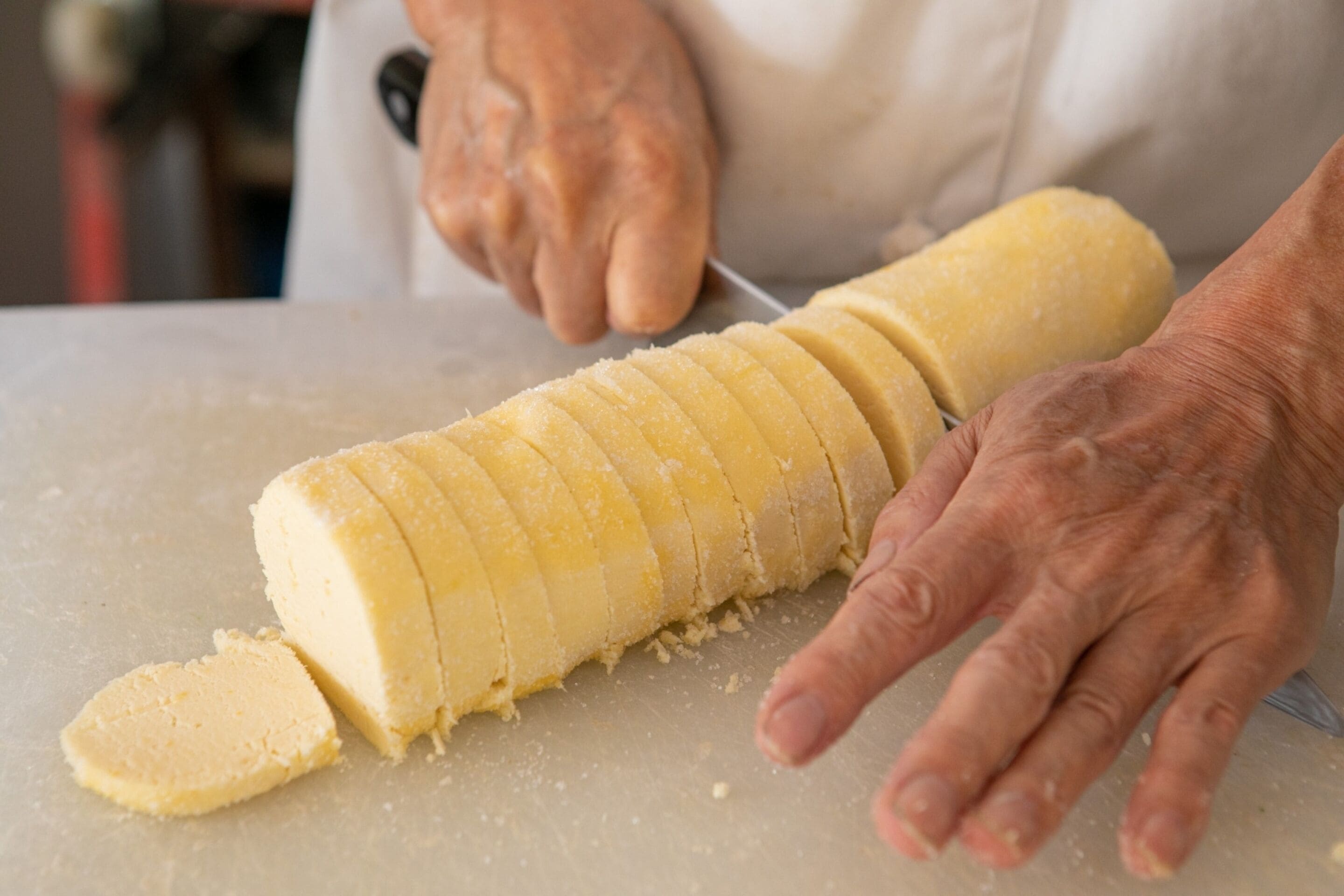 Une personne qui découpe un aliment de forme cylindrique sur une planche à découper.