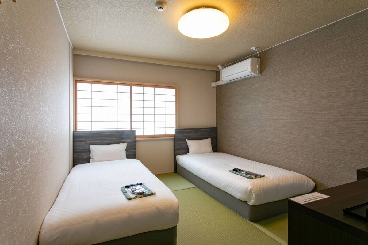 Habitación de hotel con dos camas individuales, ventana con vistas, una lámpara en el techo y un escritorio pequeño.