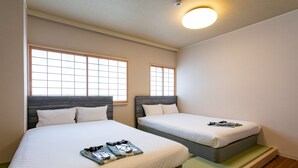 Habitación de hotel con dos camas, cada una con cabecero, ventana y mesita de noche con lámpara.