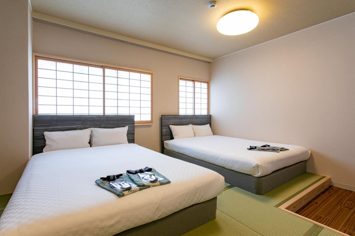 Habitación de hotel con dos camas, cada una con cabecero, ventana y mesita de noche con lámpara.