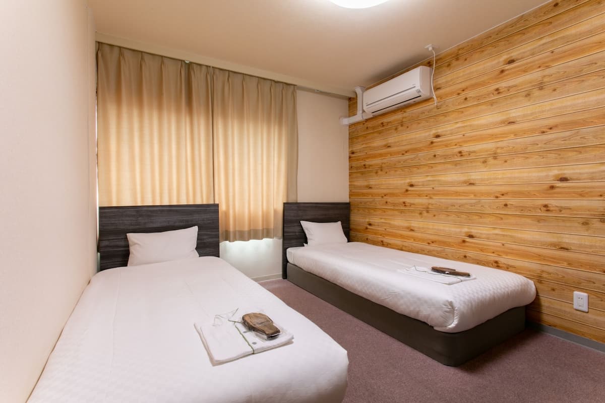 Habitación de hotel con dos camas, cortinas color beige, paneles de madera y un equipo de aire acondicionado.