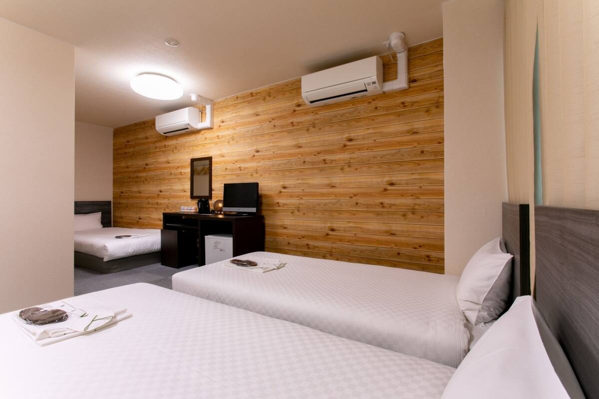 Habitación de hotel con dos camas, un escritorio con computadora, un espejo y paneles de madera en las paredes.