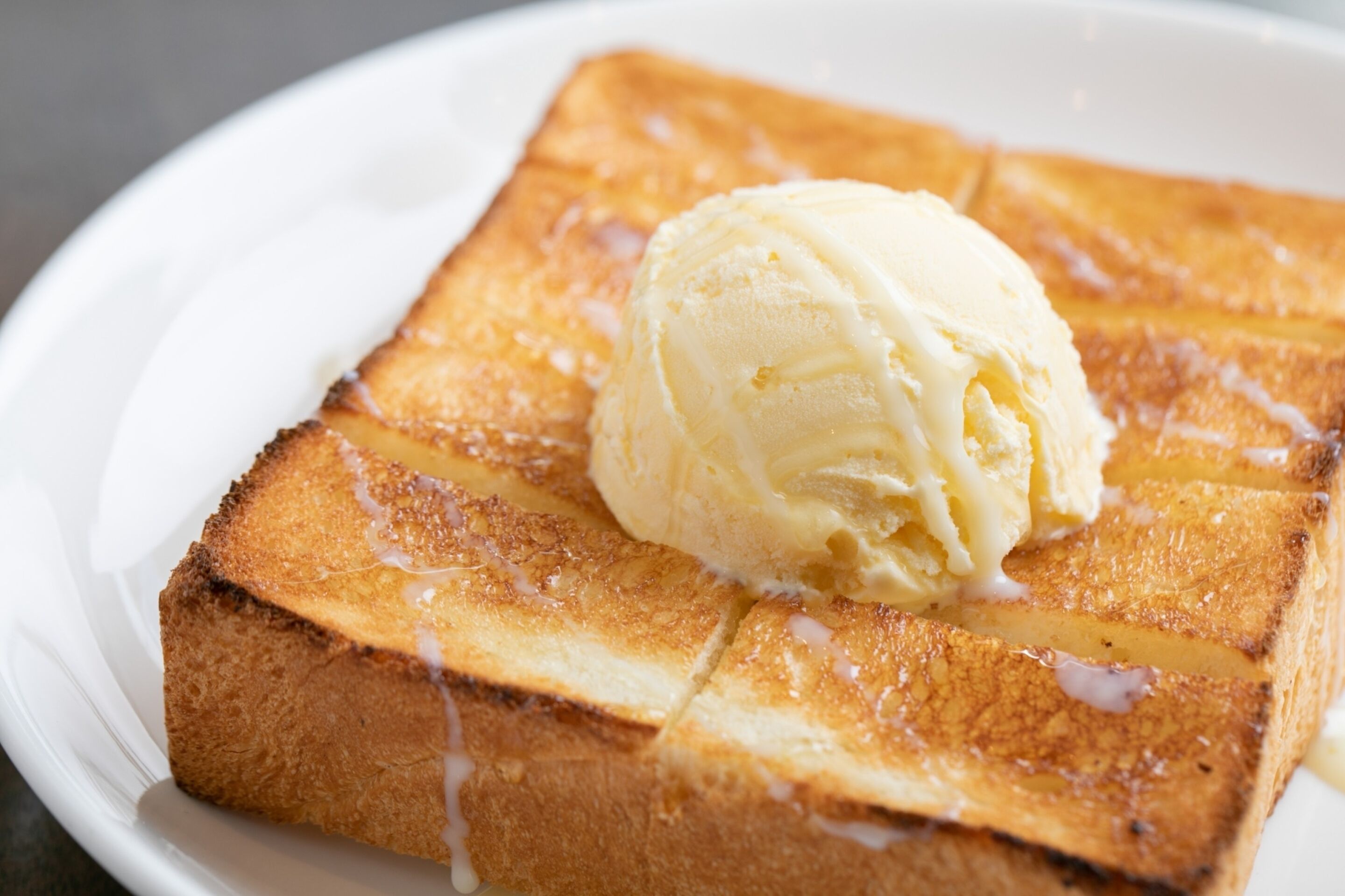 A slice of toasted bread with a pat of butter melting on top, served on a white plate.