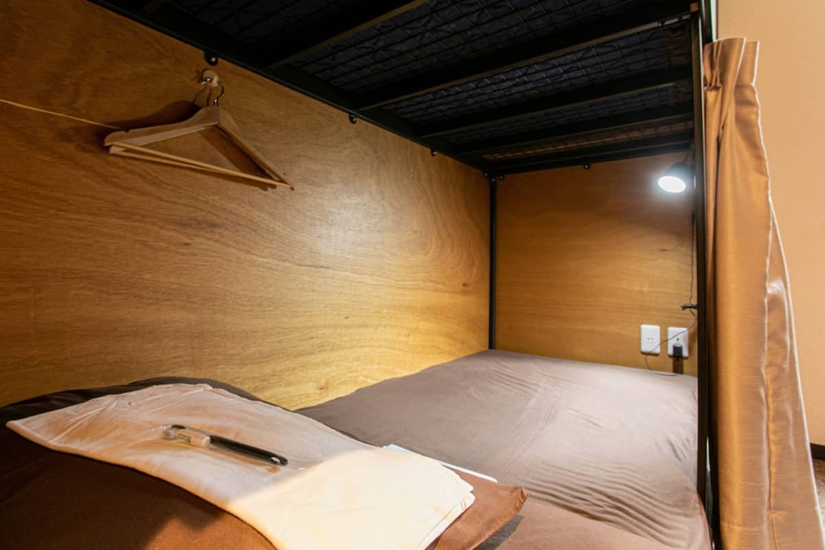 Una cama individual con cabecera de madera, un perchero y un enchufe en la pared.