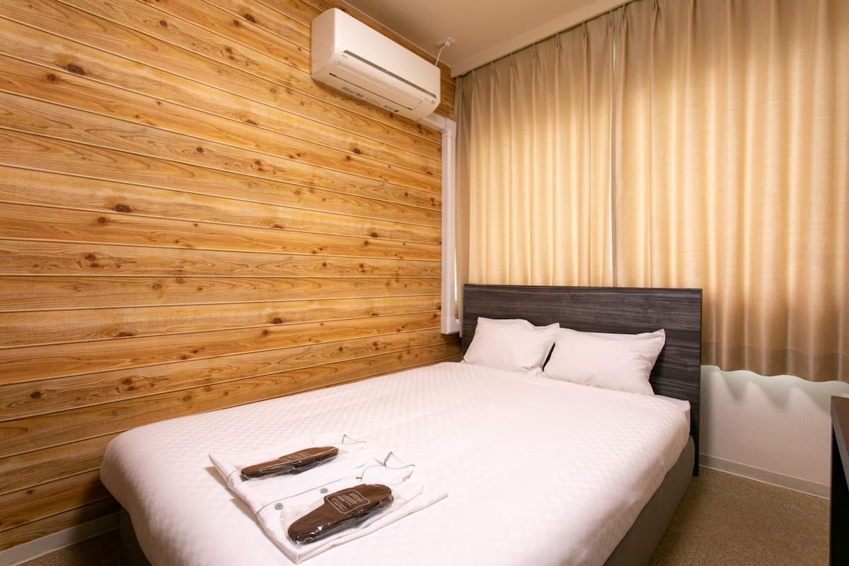Habitación de hotel con pared de madera, cama con ropa blanca y un equipo de aire acondicionado encima.