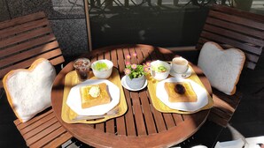 Una mesa redonda de madera con platos con forma de corazón, un bol de ensalada, una taza de café y un vaso de té helado.