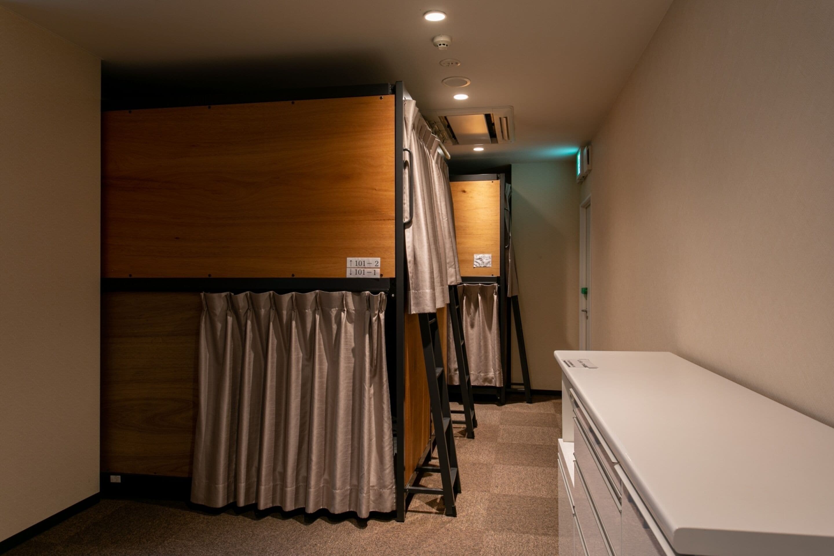Quarto de hotel com beliches, penteadeira branca e área de chuveiro.
