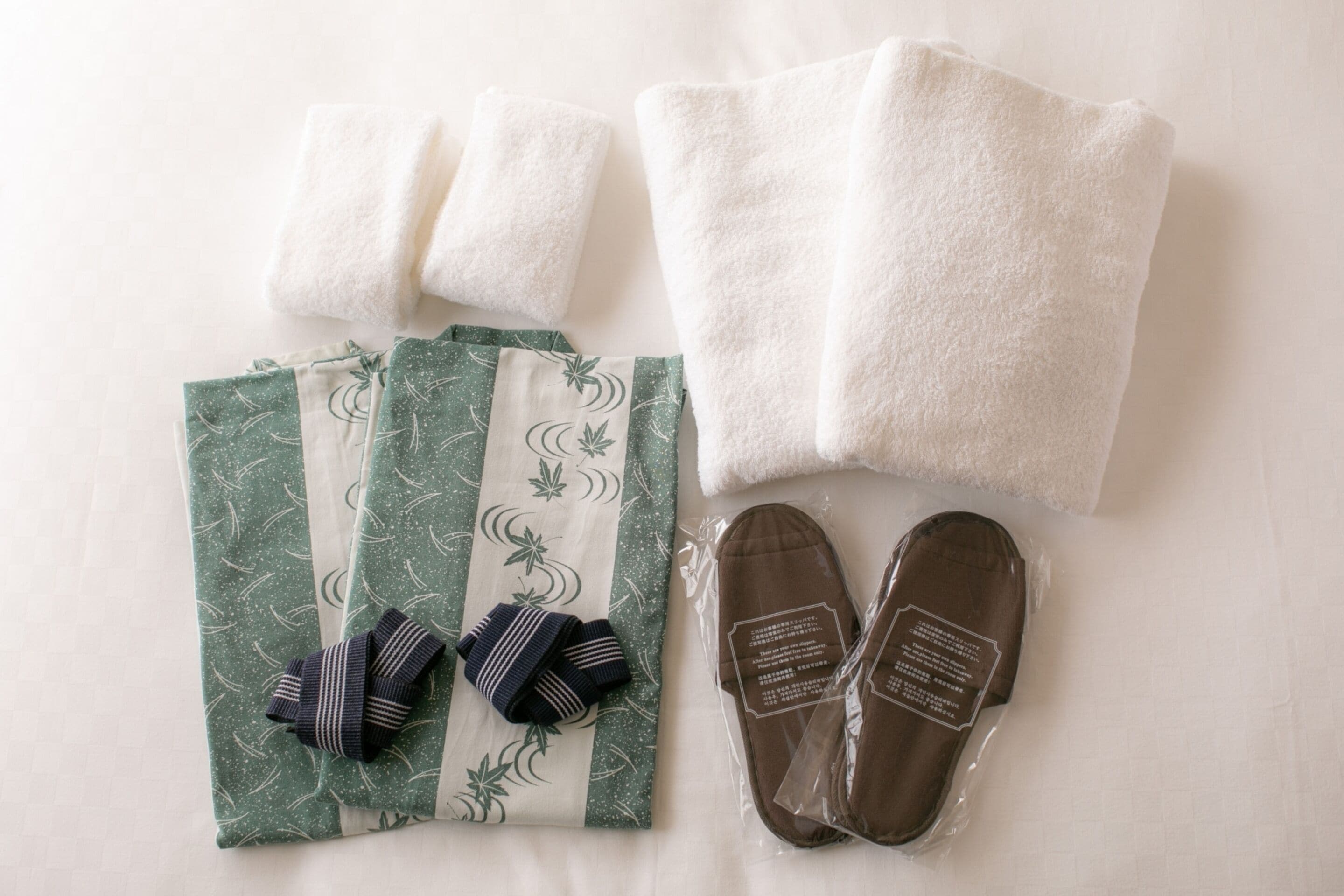 A neatly arranged set of towels, a pair of slippers, and a folded garment with a green and white pattern.