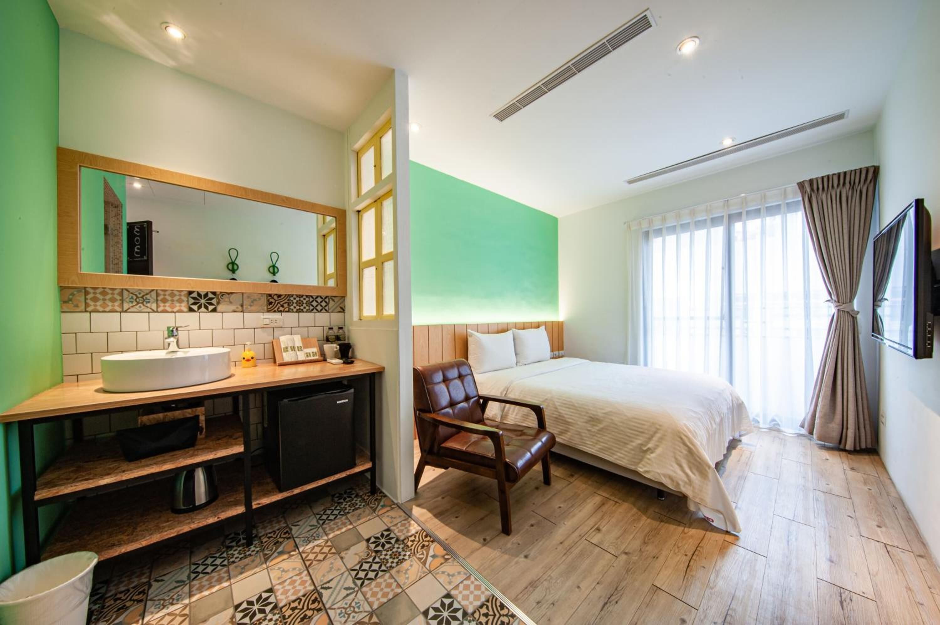 A hotel room with a large bed, a wooden desk with a sink, a chair, and a mirror.