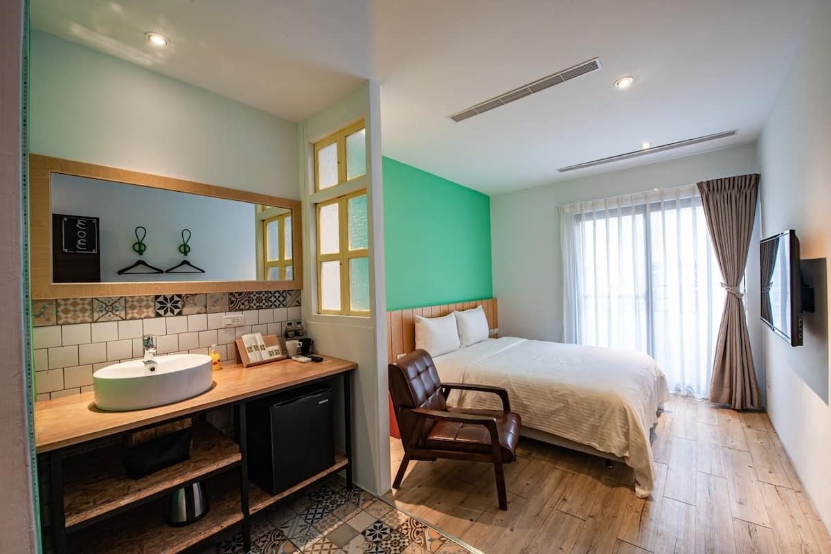 A hotel room with a bed, a desk with a sink, a chair, and a television.