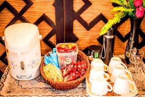 A breakfast setup with a coffee maker, tea kettle, cups, and a basket of snacks. - Patong Sino House (Patong)