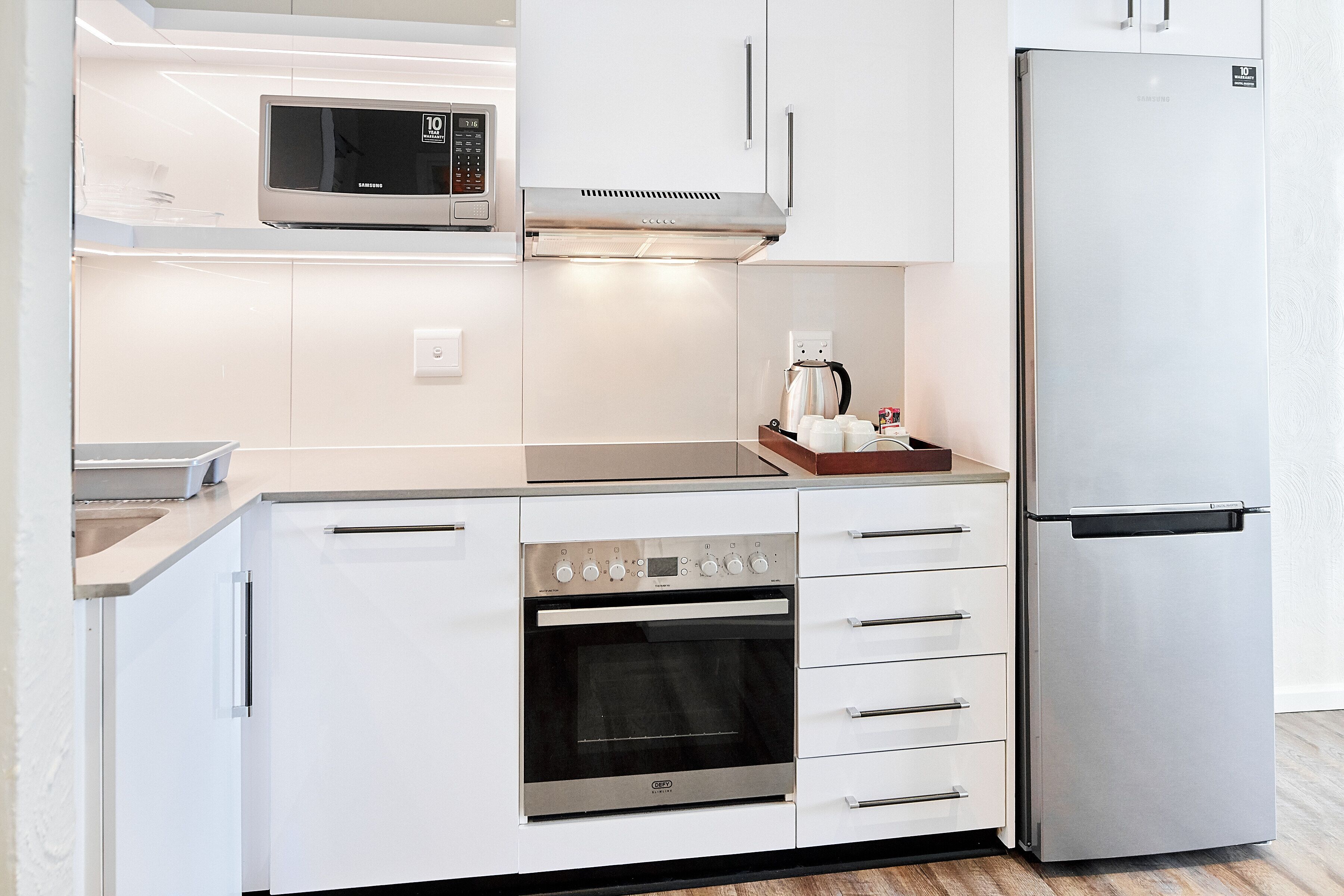 A modern kitchen with white cabinetry, a stainless steel refrigerator, a built-in microwave, and a coffee maker.
