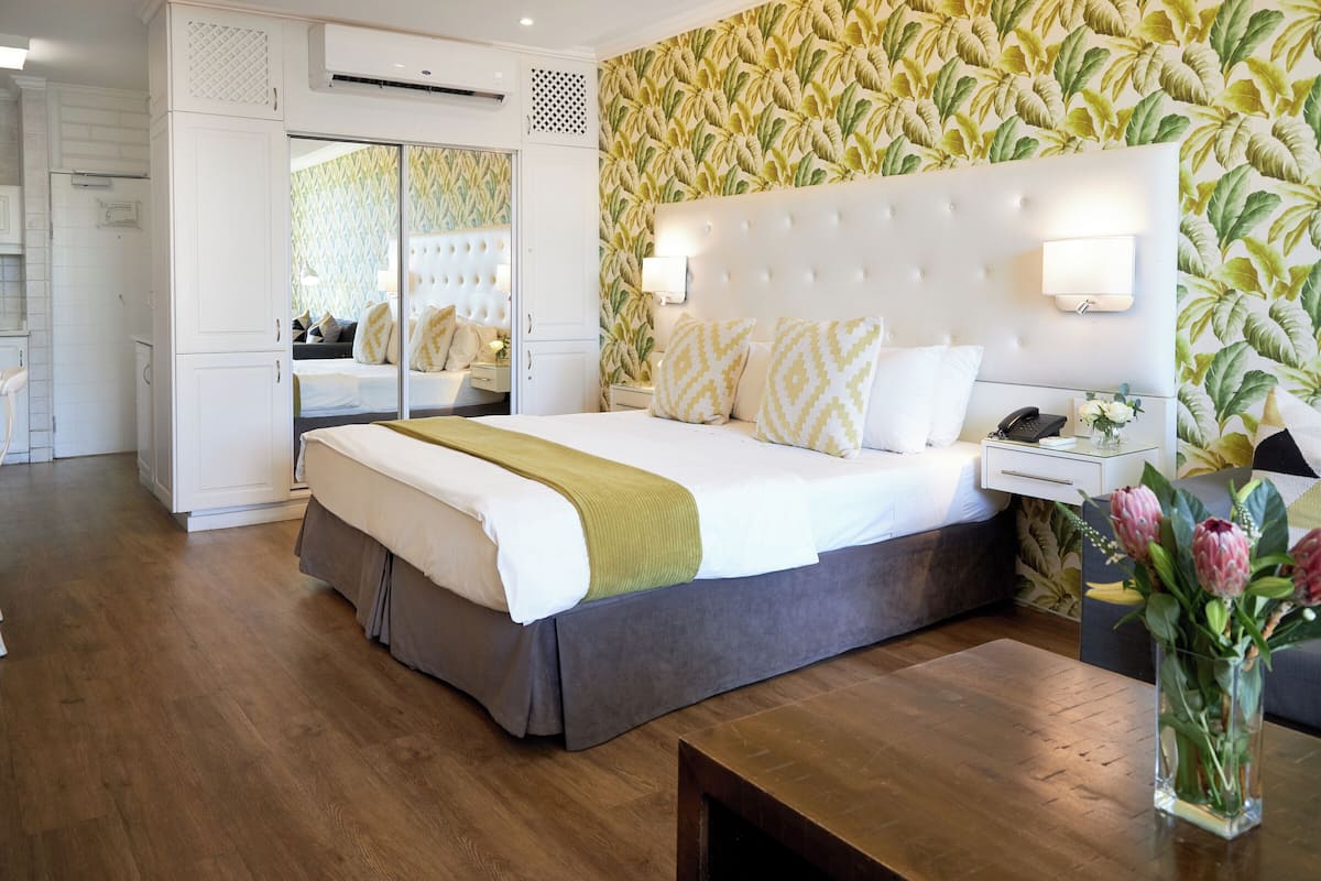 A hotel room with a large bed, a bedside table with a lamp, a nightstand with a phone, and a vase with flowers.