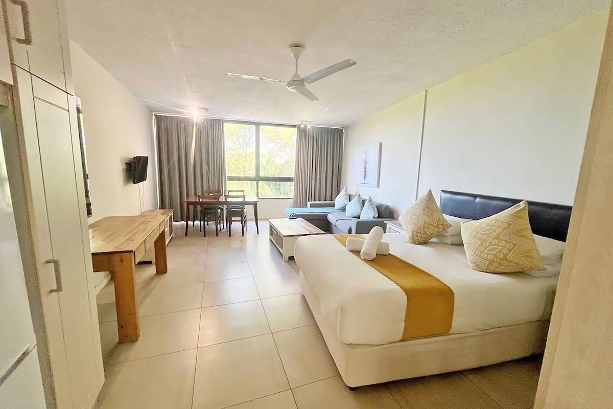 A hotel room with a bed, a desk, a chair, a sofa, and a ceiling fan.