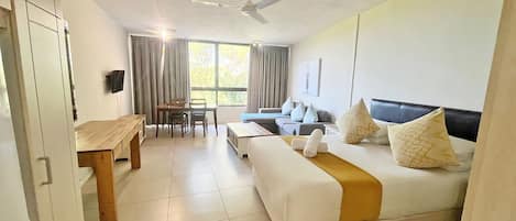 A hotel room with a bed, a desk, a chair, a sofa, and a ceiling fan.