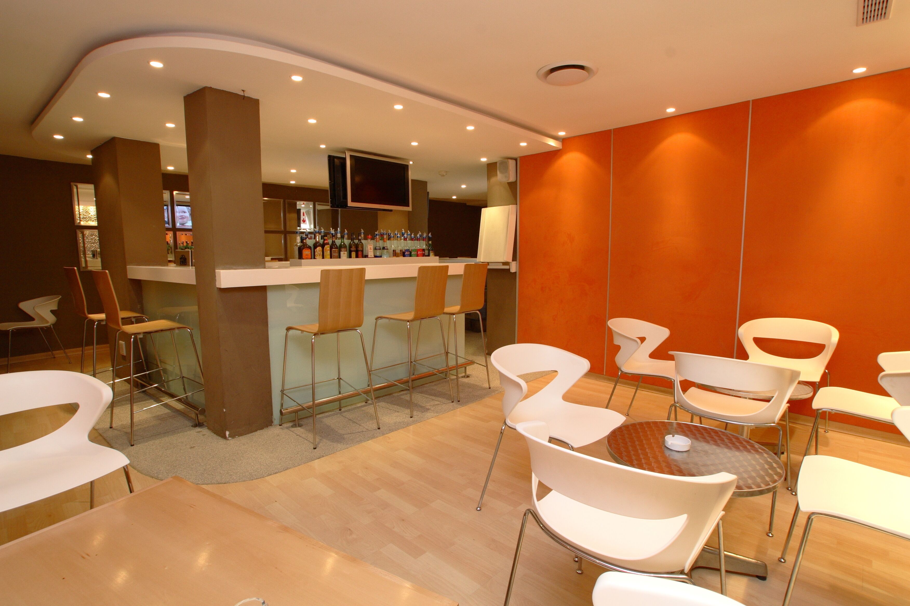A modern bar area with stools and a counter, surrounded by white chairs and tables.
