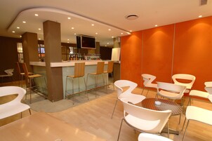 A modern bar area with stools and a counter, surrounded by white chairs and tables.