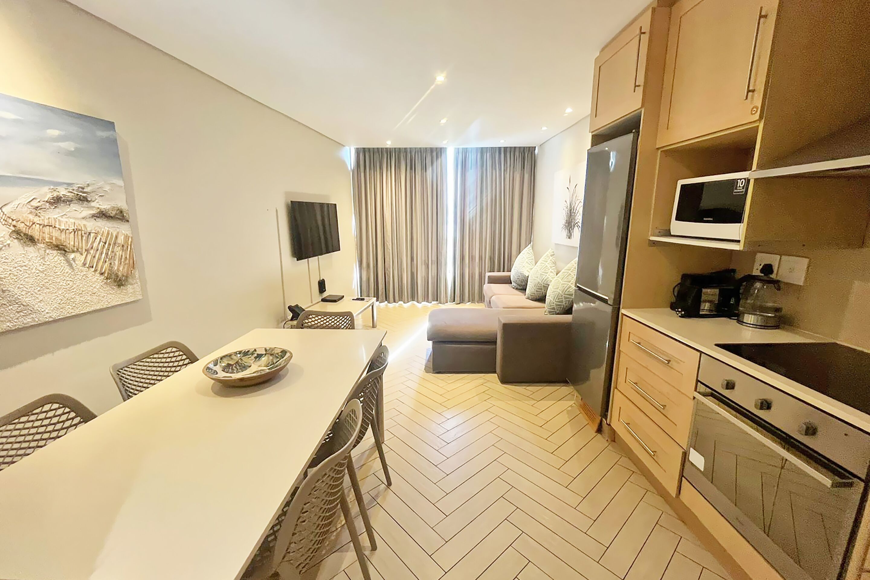Una cocina moderna con zona de comedor, televisión de pantalla plana y un amplio ventanal con cortinas.