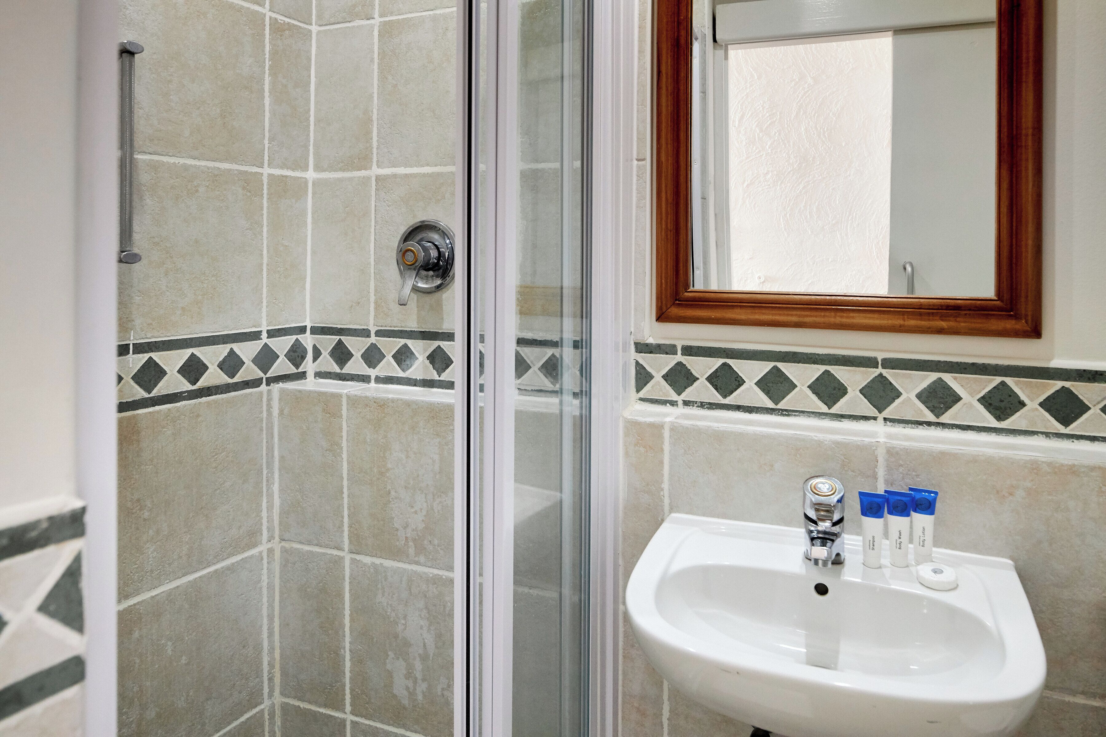 A bathroom with a glass shower enclosure, a sink with toiletries, and a mirror with a wooden frame.