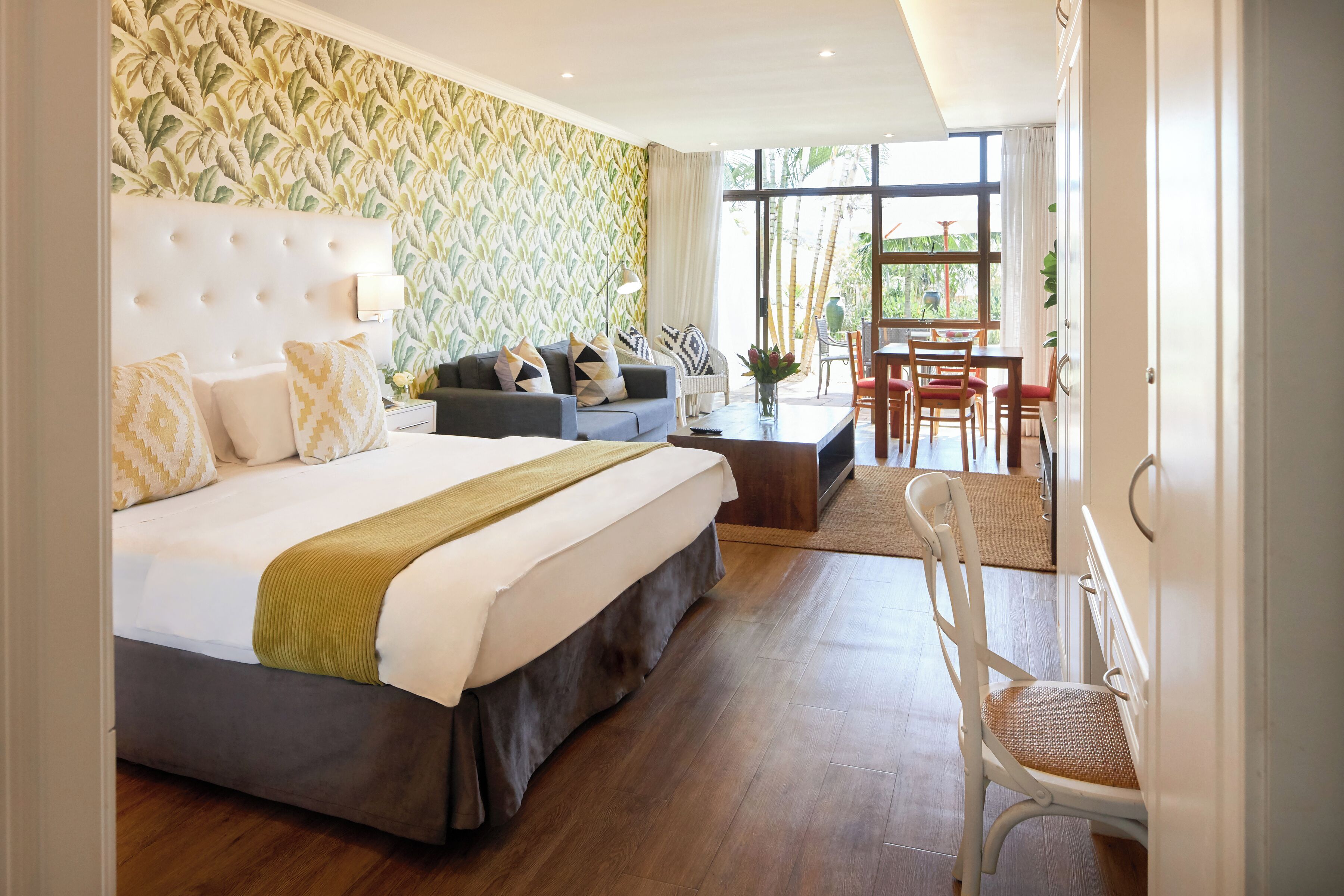 Habitación de hotel con una cama grande, un sofá, un comedor con mesa y sillas, y vistas al exterior.