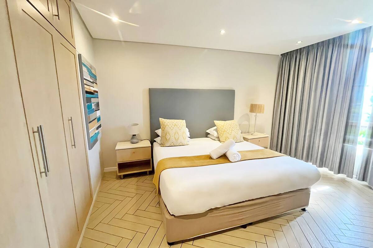 A modern hotel room with a large bed, a wardrobe, a nightstand, and a window with curtains.