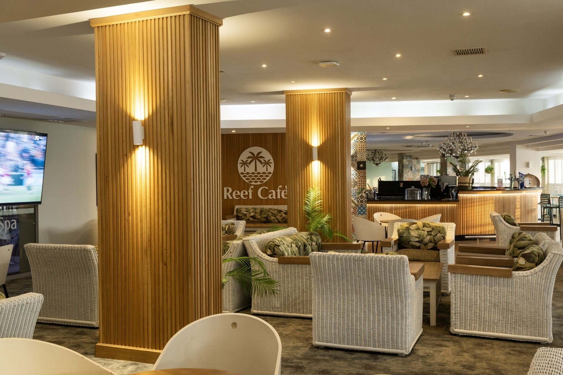Un hall con mobiliario de mimbre, una recepción y un cartel de Reef Café.