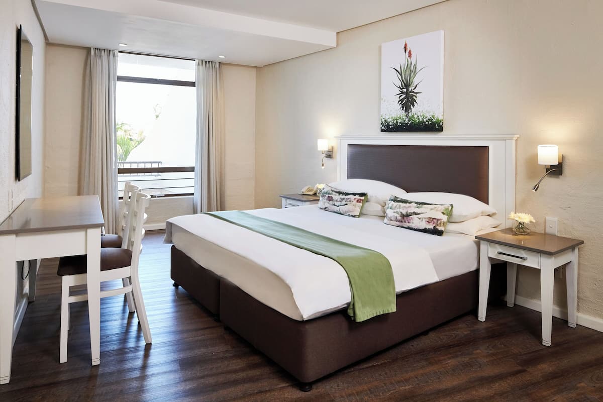 A hotel room with a bed, a desk, a chair, a nightstand, and a window with curtains.