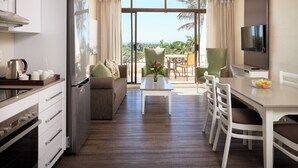 A modern kitchen with a refrigerator, stove, and cabinets. There is a dining area with a table and chairs, and a TV mounted on the wall. -  First Group Breakers Resort (Umhlanga)