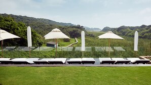 A series of sunbeds with umbrellas, a grassy area, and a view of a hilly landscape. -  First Group Breakers Resort (Umhlanga)