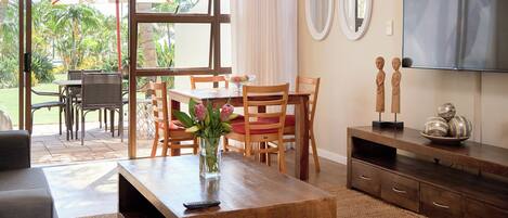 A well-lit living room with a wooden coffee table, a TV, and a dining area with chairs and a table.