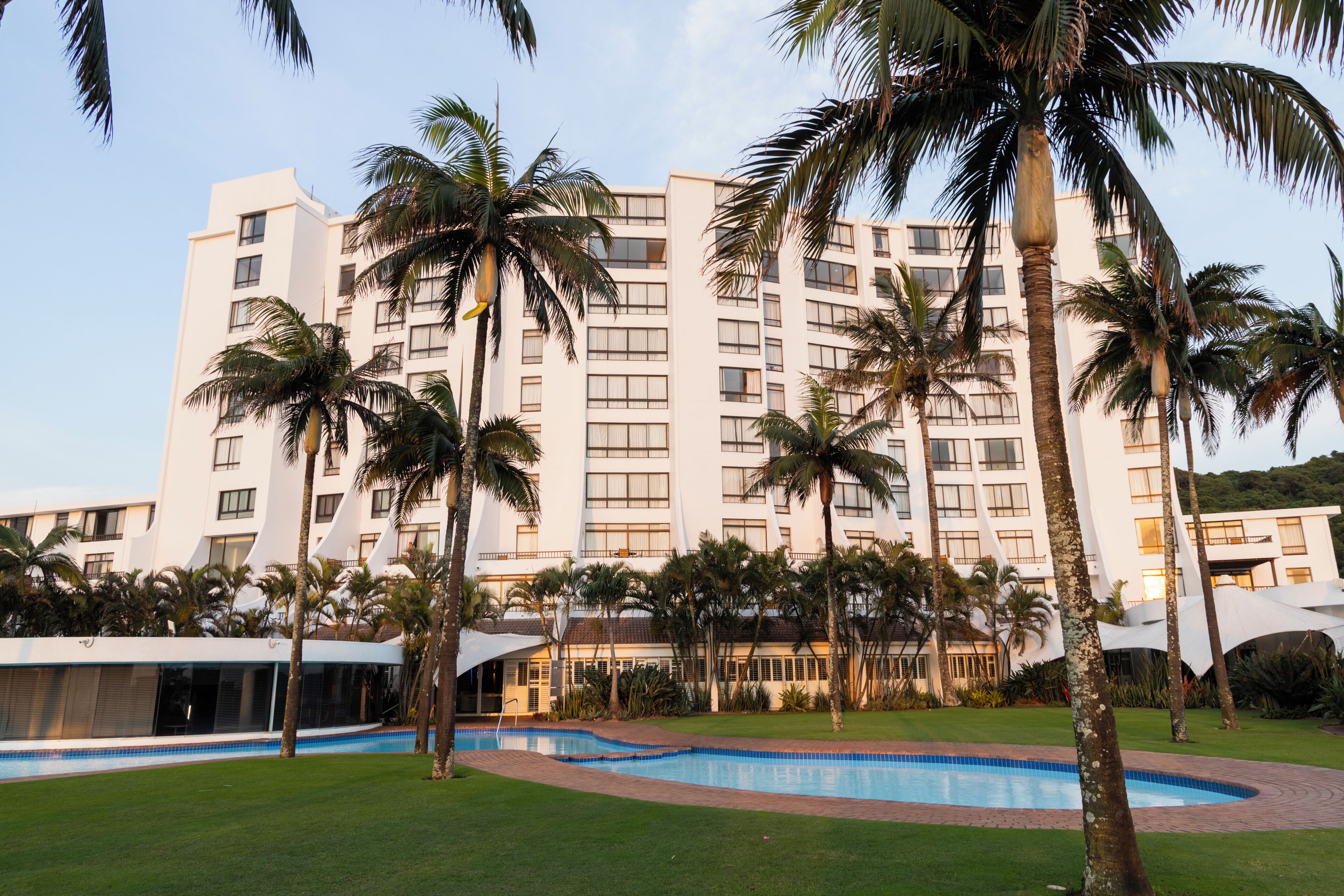 Un hôtel doté d’une piscine, de palmiers et d’une façade moderne.