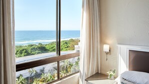 A hotel room with a large window offering a view of the ocean and greenery. -  First Group Breakers Resort (Umhlanga)