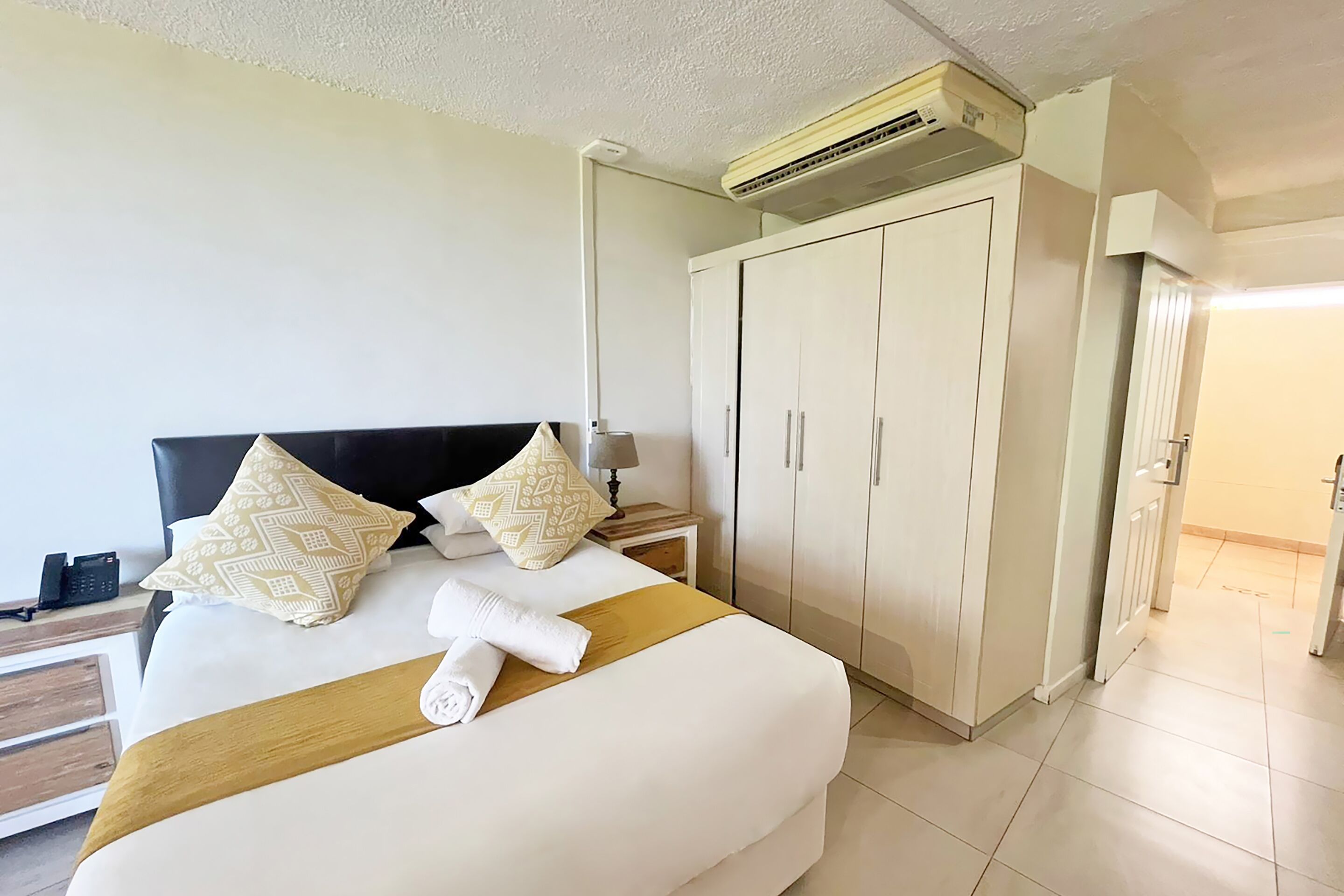 A hotel room with a bed, a wardrobe, a nightstand, and an air conditioning unit.