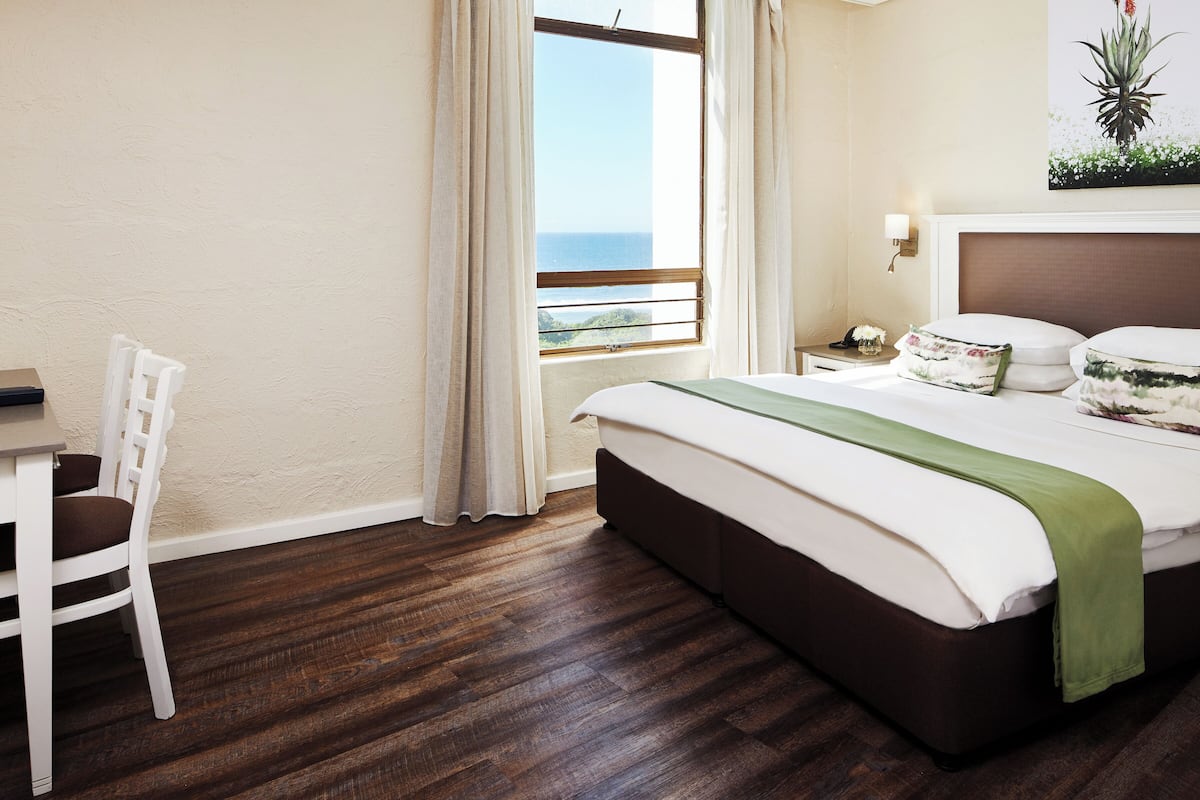 A hotel room with a bed, a chair, a nightstand, and a window with a view.