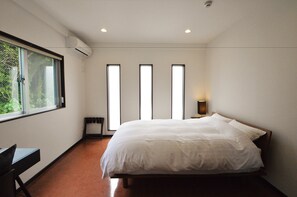A bedroom with a large bed, a desk, and a window.