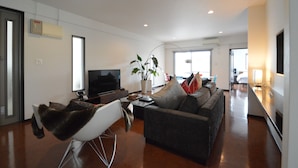 A modern living room with a sofa, a chair, a television, and a plant. - The White Reef (Uruma)