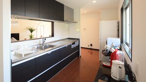 A modern kitchen with dark cabinets, a stainless steel sink, and a built-in oven. - The White Reef (Uruma)