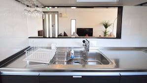A modern kitchen with a stainless steel sink, a dish rack, and a flat-screen TV mounted above the sink. - The White Reef (Uruma)