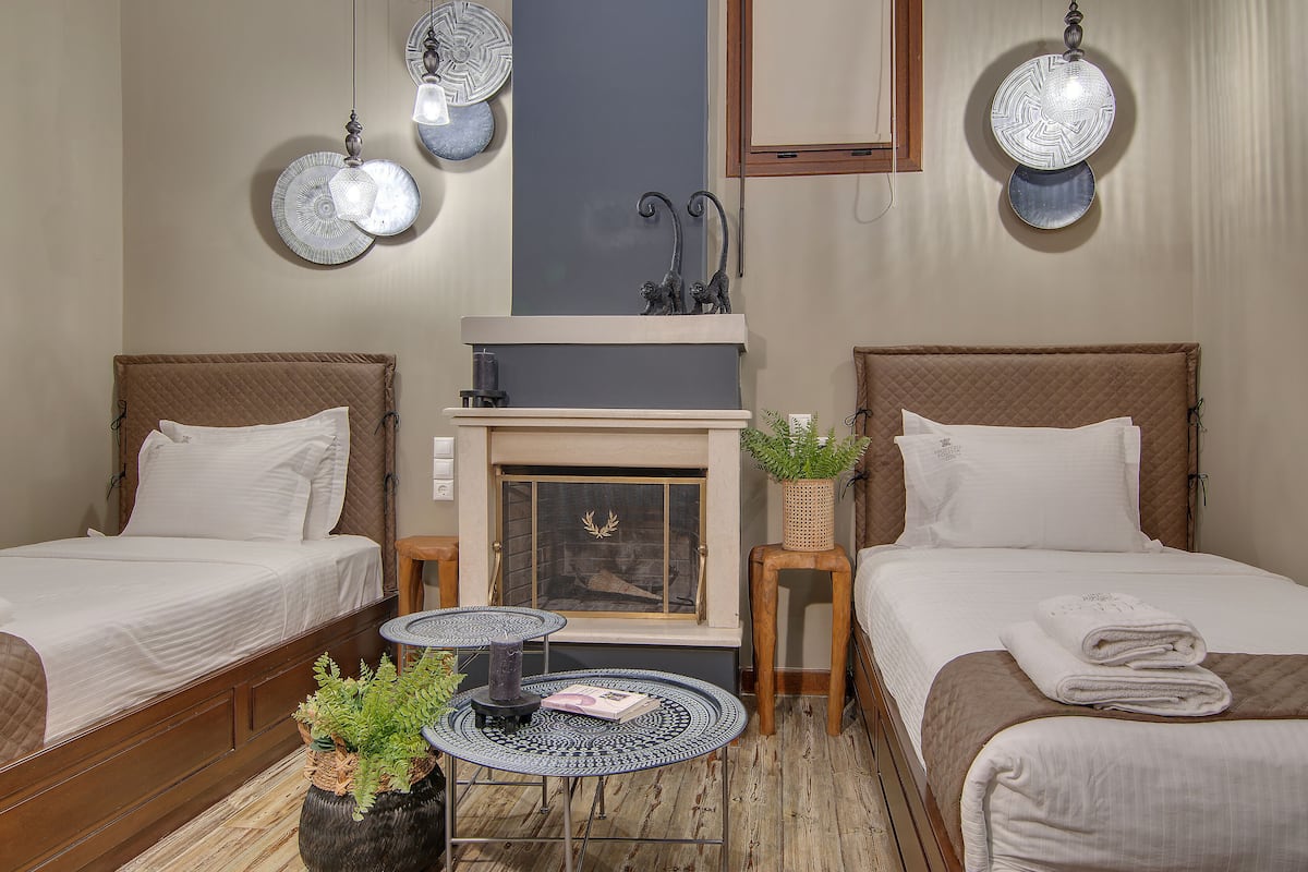 A room with two beds, a fireplace, and a small table with a book and plants.