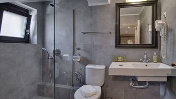 Un baño moderno con ducha envuelta en vidrio, inodoro, lavamanos con espejo y artículos de aseo sobre el lavamanos.