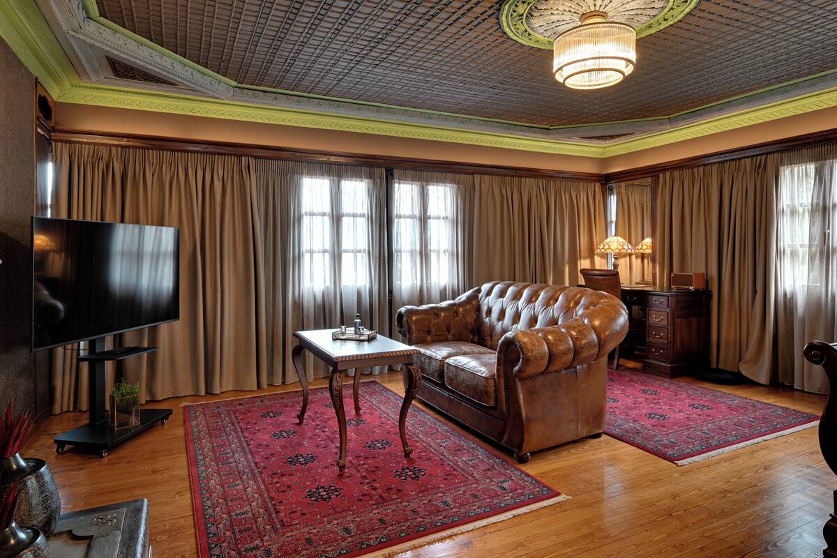 A room with a leather sofa, a television, a table, and a patterned rug.